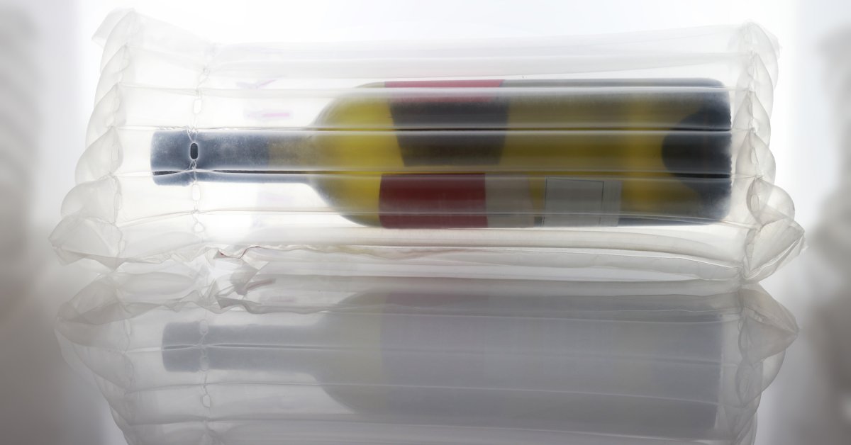 A close-up view shows a single, green wine bottle lying on its side wrapped in a clear, plastic bubble wrap.