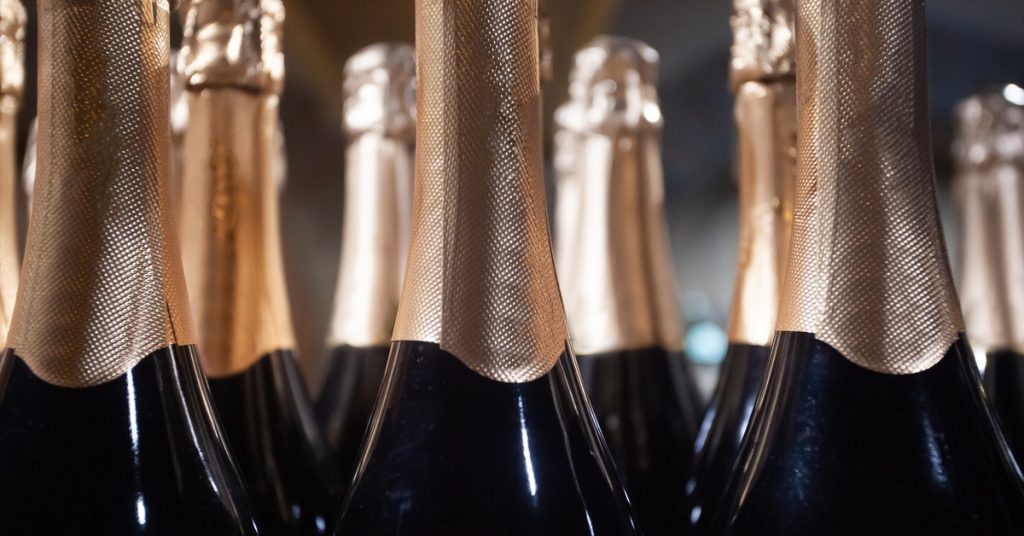 A close-up of dark champagne bottles with with a golden wrapping around their necks in a low-lit space.