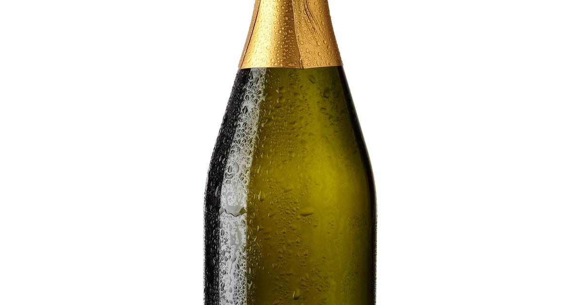 A bottle of champagne with condensation on it, gold foil around the top, and no label on the body against a white background.