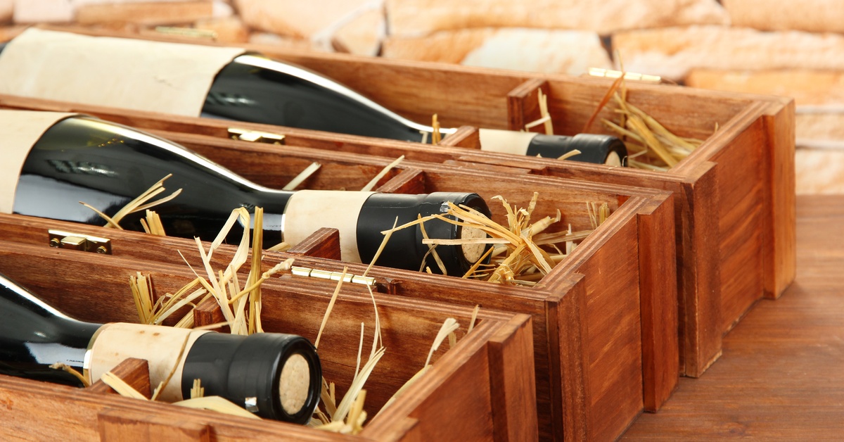 Three wooden wine boxes packed with paper shreds to protect the dark-colored, sealed bottles in the boxes.