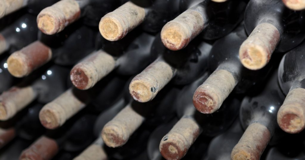 Several dusty bottles of wine arranged on top of each other with their tops pointing out, covered in wax.