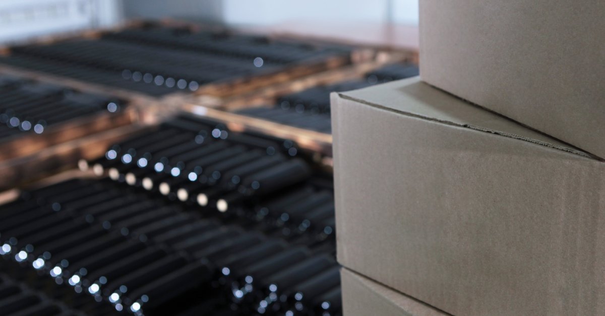 A stack of cardboard boxes in the foreground with an array of wine bottles out of focus in the background.