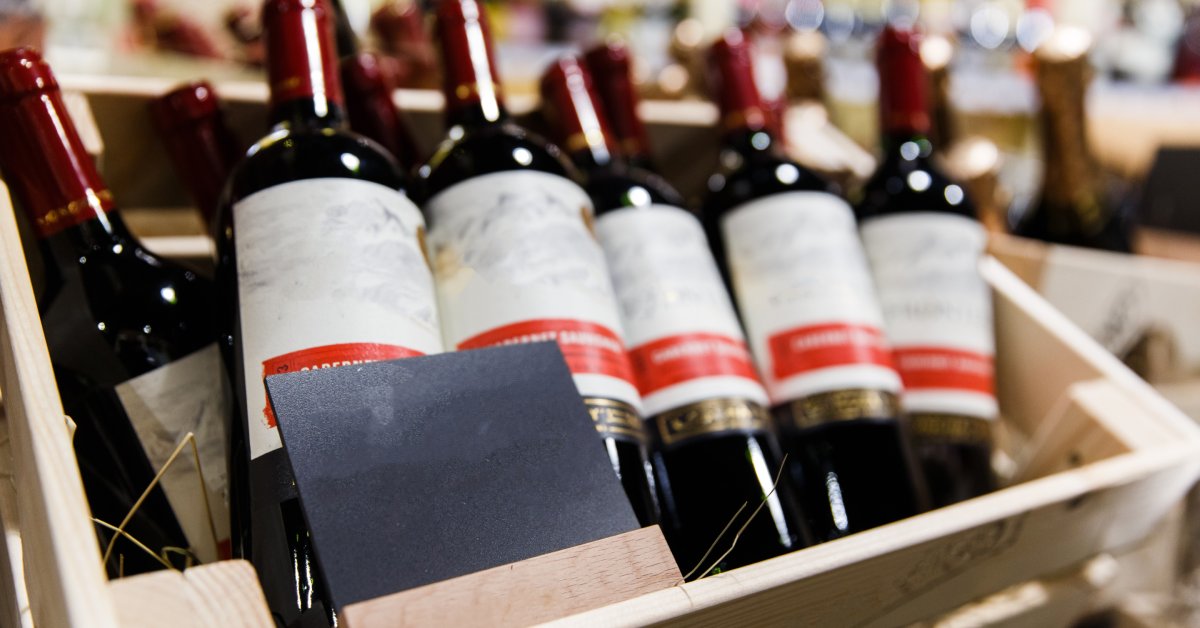 Several bottles of red wine arranged in a wooden box with textured but blank labels and a black card resting in front of them.